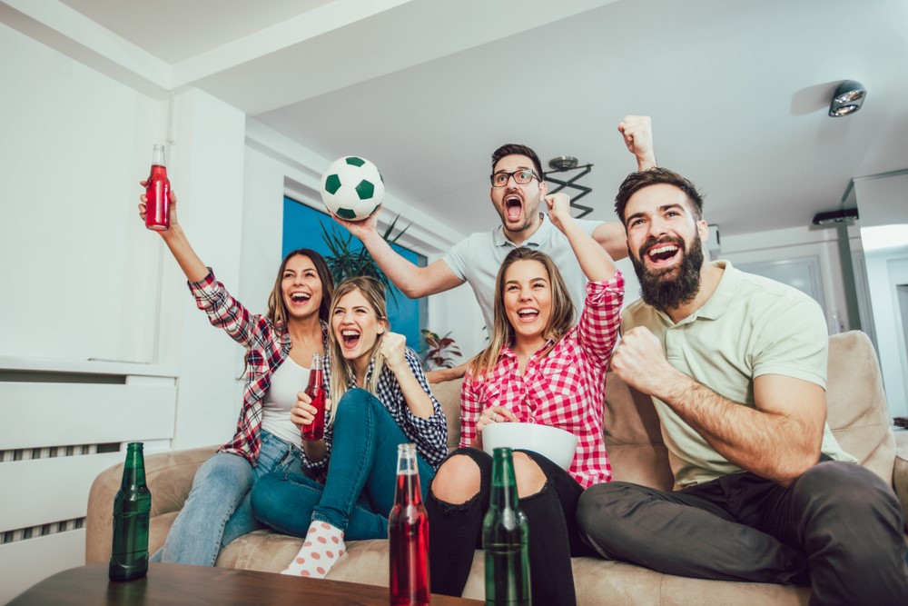 Fußballfans sitzen auf einem Sofa und verfolgen ein Fußballspiel